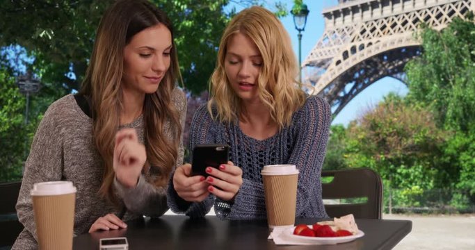 Lovely blonde girl socializing with friend and sharing smartphone pictures in front Eiffel Tower in Paris, France, Two cute girls using cell phone to look at pictures near French landmark, 4k