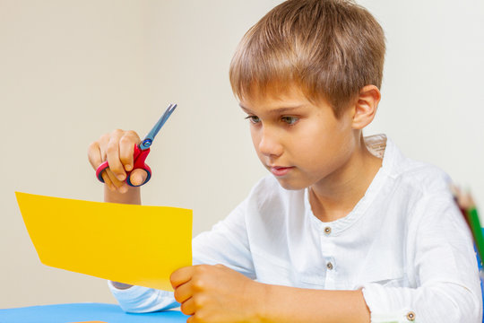 Child Cutting Colored Paper With Scissors At The Table