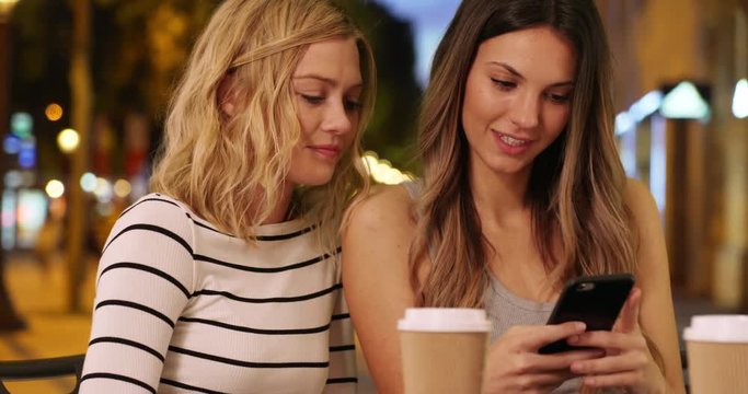 Close up of pretty brunette woman showing blonde friend smart phone in Champs Elysees Avenue in Paris, France, Close view of two friends sharing smartphone in European city, 4k