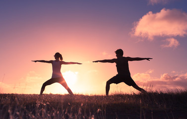 Man and woman practicing yoga stretches at sunset in a open field.