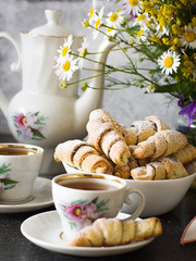 Croissants (bagels) with poppy seeds and tea on a bouquet of flowers field background. Morning tea with croissants.