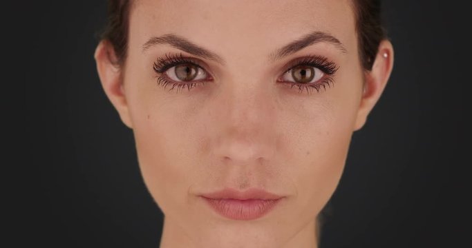 Portrait of pretty brunette gazing at camera seriously on solid dark gray backdrop, Frontal view of attractive woman looking at the camera on dark background, 4k