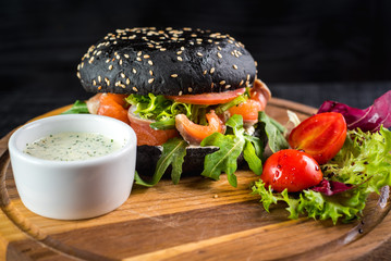 Tasty black burger with salmon on wooden background