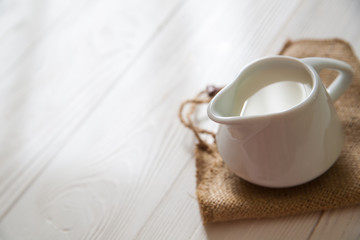  White milk pitcher on a white wooden background. Jug of milk. Farmhouse. Rustic. Sunlit. Copy space.