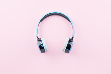 Blue wireless headphones close up on pastel pink background. Flat lay, top view