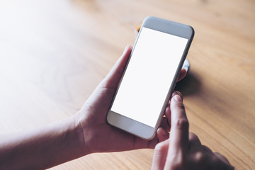 Mockup image of hands holding white mobile phone with blank desktop screen on wooden table