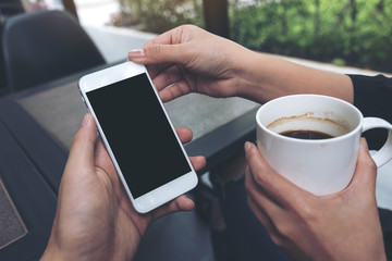 Mockup image of two people looking and holding a white mobile phone with blank black desktop screen while drinking coffee in cafe
