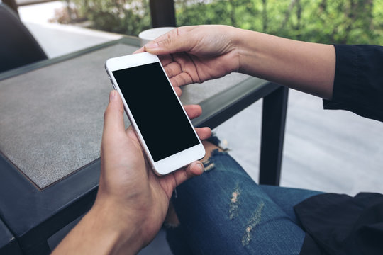 Mockup image of two people looking and holding a white mobile phone with blank black desktop screen in cafe