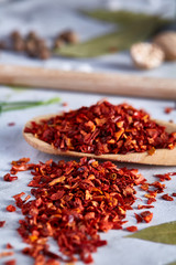 Red hot chillies pepper flakes in wooden spoon on white textured background, top view, close-up, selective focus.