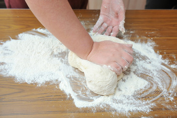 Women's hands knead the dough in the kitchen on the table. Close-up