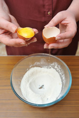 Female hands separate the egg white from the yolk over a bowl of wheat flour in the kitchen