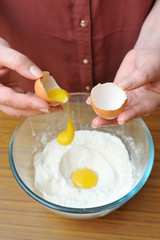 Female hands separate the egg white from the yolk over a bowl of wheat flour in the kitchen