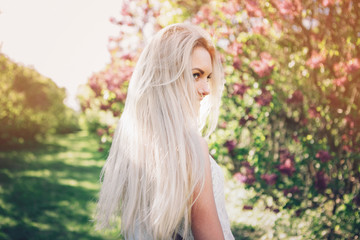 Woman with  long blond hair in the garden with flowers. Beautiful girl on a sunny day.