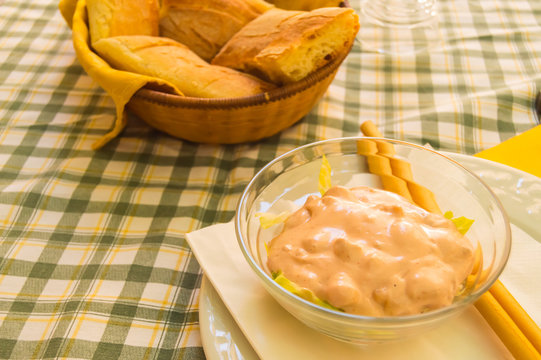Shrimp cocktail in a glass bowl with breadsticks own on an orange napkin on a white plate