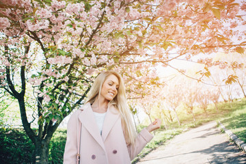 Young beautiful woman in a pink coat posing with flowers in  garden. Park.