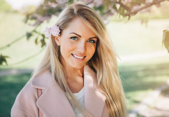 Young beautiful woman in a pink coat posing with flowers in garden. Park.