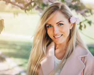 Young beautiful woman in a pink coat posing with flowers in  garden. Park.