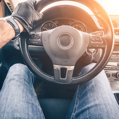 A strong man's hand in a black glove holds the steering wheel driving a car, a first-person view from the driver's seat