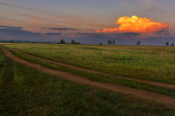 Obraz premium Green field, road, blue sky and clouds