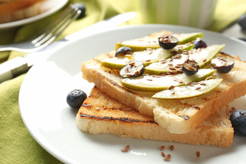 Tasty sweet toasts with sliced pear and blueberry on plate, closeup