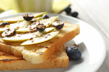 Tasty sweet toasts with sliced pear and blueberry on plate, closeup