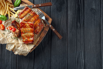 Wooden board with delicious grilled ribs and french fries on table