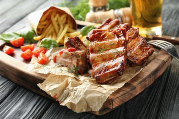Wooden board with delicious grilled ribs on table