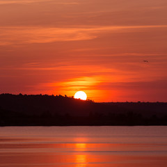 red sunset, the sun touched the coastline, the sun reflected in the water, a lot of sky, the concept nature and summer