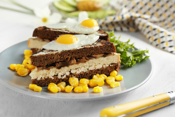 Plate with toasted bread, fried eggs and corn kernels on table