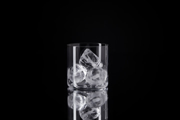 single glass with ice cubes on reflective surface isolated on black