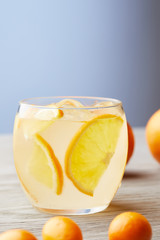 close-up shot of glass of fresh lemonade with ripe oranges on wooden surface