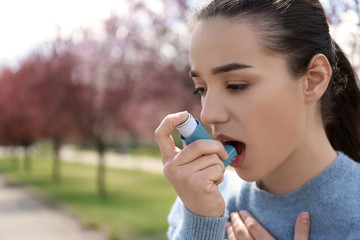 Young woman using inhaler near blooming trees. Allergy concept