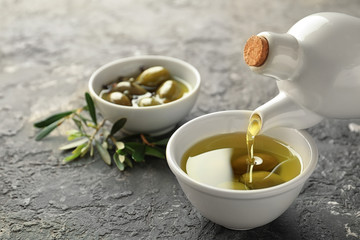 Pouring of fresh oil into bowl with olives on table