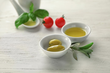 Bowls with oil and olives on white wooden table