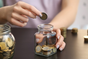 Woman putting coins into glass jar on table. Savings concept