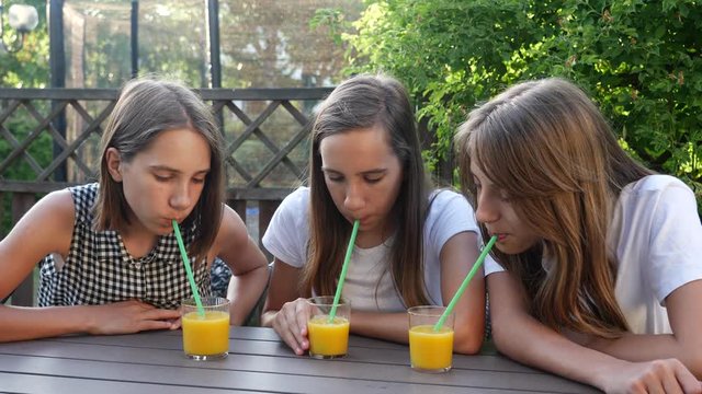 Drinking juice sitting at terrace table teenager sisters girls triple twins having fun