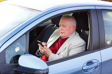 Older businessman sitting on car driver seat and read or write SMS by SmartPhone. People and technology concept