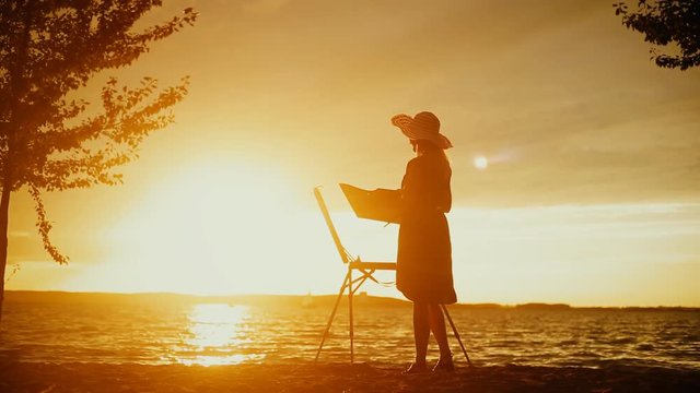 Painter in a summer hat making a picture closeup at sunset silhouette