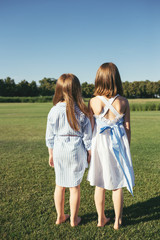 Two girls standing and turned their backs on the field. Sisters.