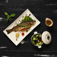 Grilled salmon served with lettuce leaves, cherry tomatoes and lemon slices on flat rectangular plate standing on blue aged wooden surface. Low-calorie, healthy and delicious fish recipe. Top view.