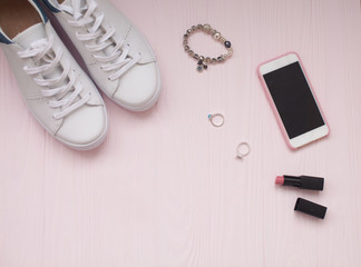 Fototapeta na wymiar women's accessories - bag, sneakers, earrings, rings, lipstick on wooden pink background, top view