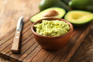 Bowl with tasty guacamole and ripe avocado on wooden board