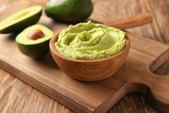 Bowl with tasty guacamole and ripe avocado on wooden board