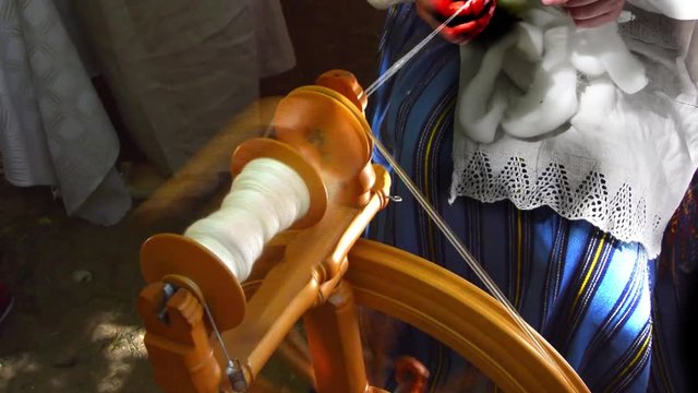 The woman in the Latvian national suit spins white woolen thread on an ancient wooden distaff