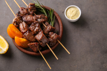 Plate with juicy meat on barbecue skewers and sauce on table