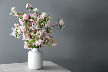 Vase with beautiful blossoming branches on table against grey background