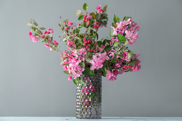 Vase with beautiful blossoming branches on grey background