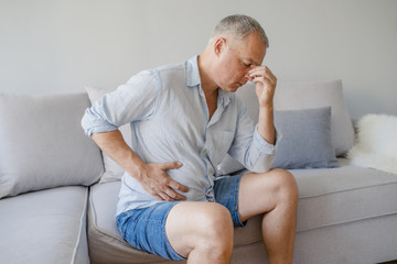 Terrible stomachache. Frustrated handsome young man hugging his belly and keeping eyes closed