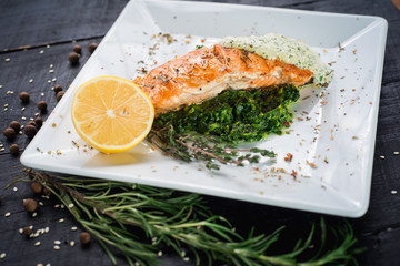 Delicious fish steak with sauce and herbs on wooden background