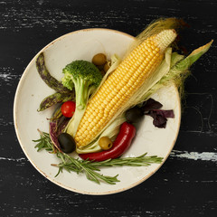 Fresh raw vegetables on round ceramic plate standing on blue aged wooden surface. Top view.